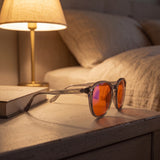 Aura blue light glasses on a bedside table beside a book and warm lamp
