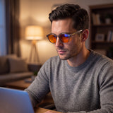 Man wearing Aura blue light glasses while working on a laptop in the evening, orange lenses