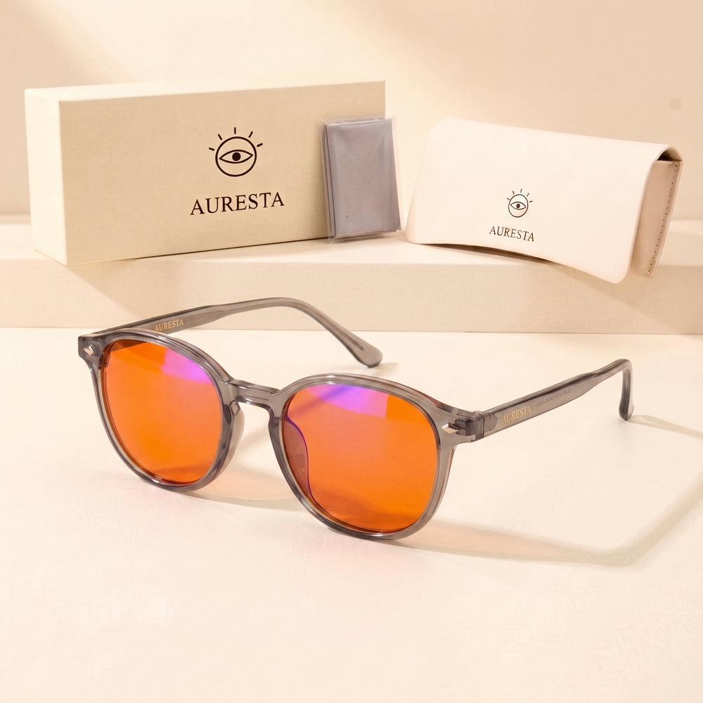 Aura blue light glasses — grey translucent TR90 frame with orange lenses next to the Auresta gift box, leather case and cleaning cloth