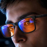 Close-up of a man wearing Ember blue light glasses, screen light reflecting across the orange lenses