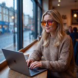 Woman working on a laptop in a cafe wearing Auresta Hazel tortoise round blue light glasses with orange lenses