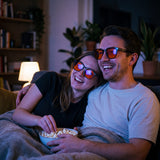 Couple on a sofa at night wearing Auresta blue light glasses, orange lenses catching the screen light