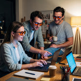 Three colleagues working late at a shared desk wearing Auresta blue light glasses with warm orange lenses
