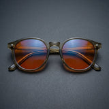 Folded Vesper blue light glasses shot head-on, showing round sage frame and warm orange lenses
