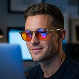 Man at a dim desk wearing round Vesper blue light glasses, monitor light reflecting in the lenses