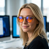 Woman in a bright office wearing Vesper blue light glasses, sage round frame with orange lenses catching the screens